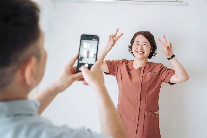 笑顔でピースサインをするスタッフをスマートフォンで撮影する様子